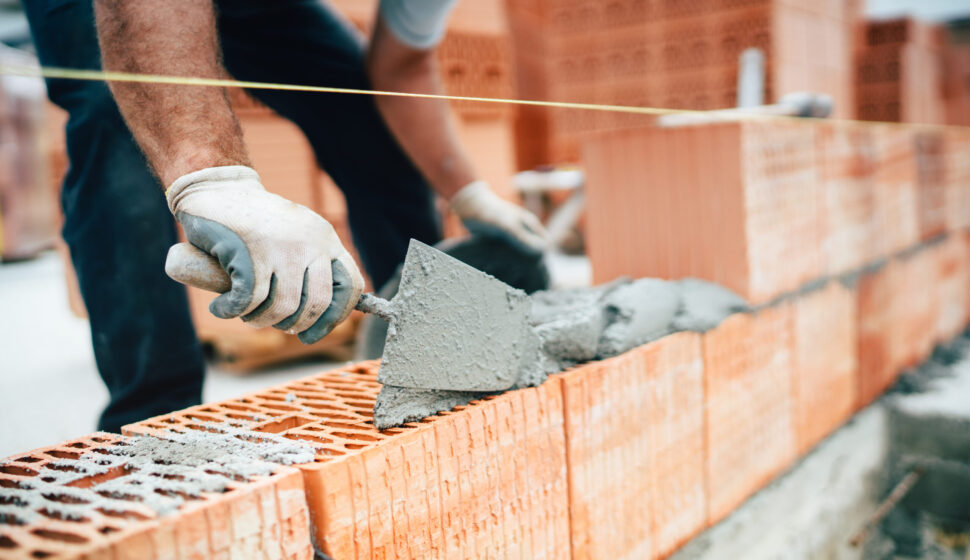 Professional worker using pan knife for building brick walls with cement and mortar